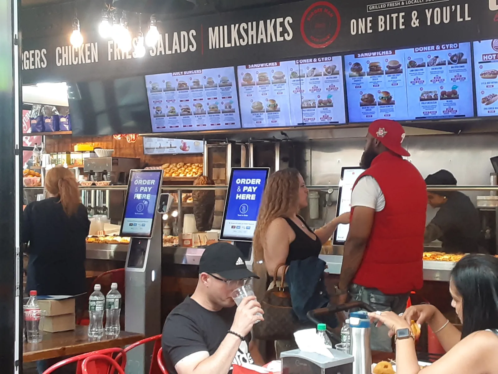 Guests self-ordering at a row of INFI kiosks during a lunch rush